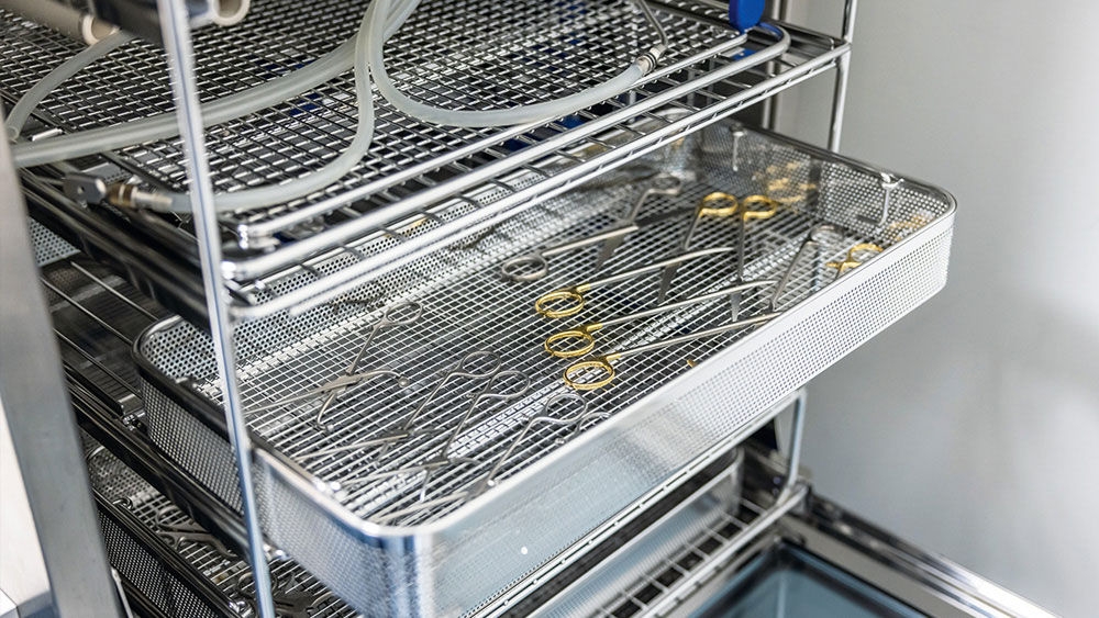 AESCULAP-Metalltabletts mit chirurgischen Instrumenten, die in einer Edelstahl-Sterilisationseinheit platziert sind.