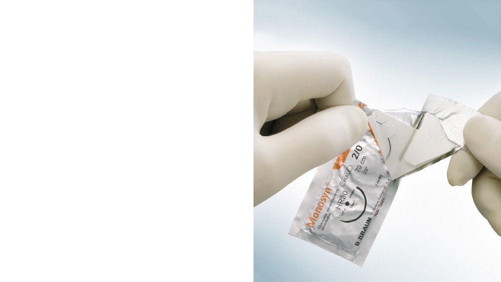 Behandschuhte Hände öffnen eine Monosyn® Nahtverpackung, indem die sterile Blisterverpackung auseinandergezogen wird, wobei das Produktetikett sichtbar ist, vor einem hellblauen Hintergrund