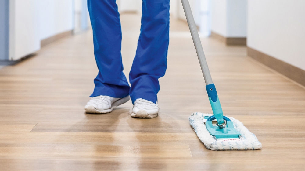 Eine tiermedizinische Fachangestellte in medizinischer Arbeitskleidung wischt mit einem Flachmopp den sauberen Flurboden als Teil routinemäßiger Reinigungs- und Hygienemaßnahmen in einer medizinischen bzw. tierärztlichen Einrichtung.