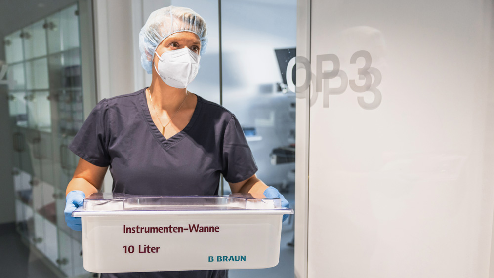 Alt Text: Person in technischer Servicekleidung handhabt einen Aesculap-Sterilisationscontainer in einem klinischen Arbeitsbereich.