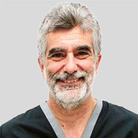 Porträtfoto mit Oberkörperansicht einer Person in dunkler medizinischer Kleidung vor hellem Hintergrund.